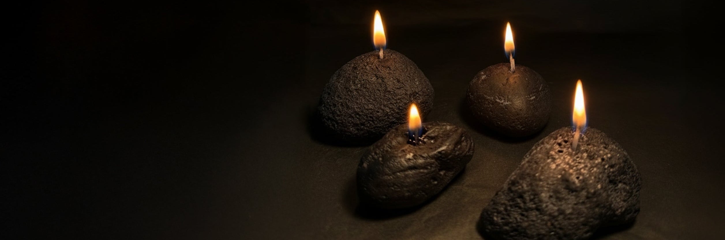 Four volcanic stone candles with lit wicks arranged on a dark surface