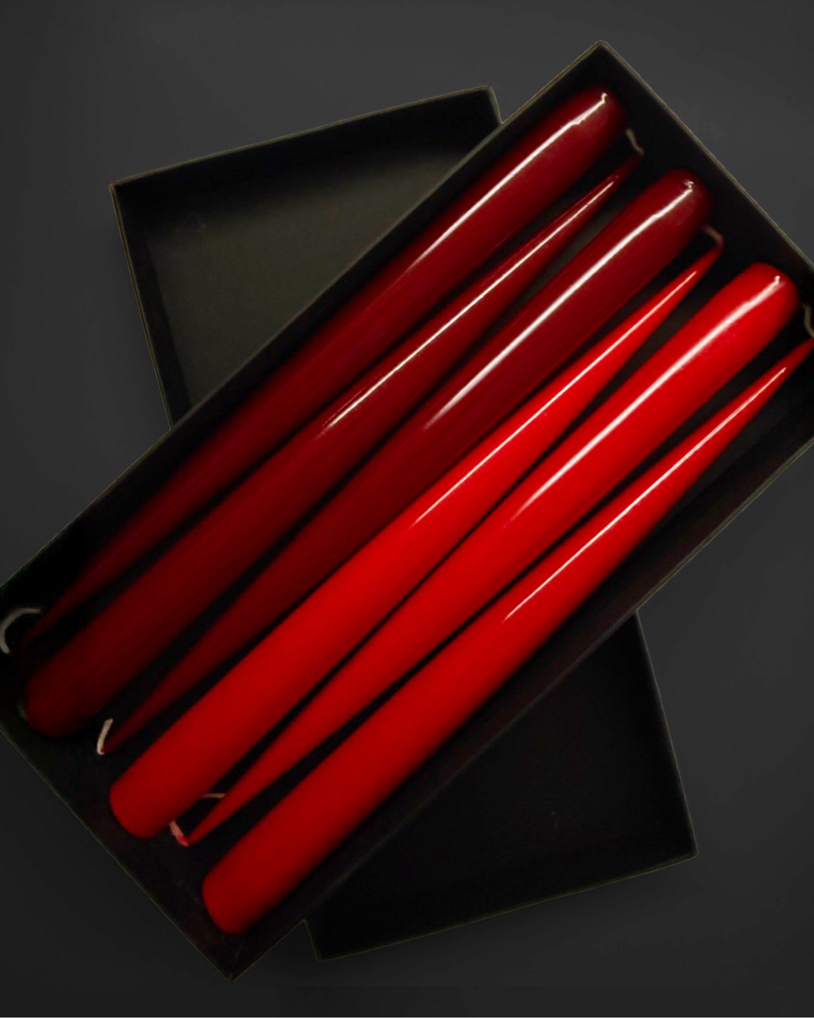 Set of red and burgundy taper candles in a black box on a dark background