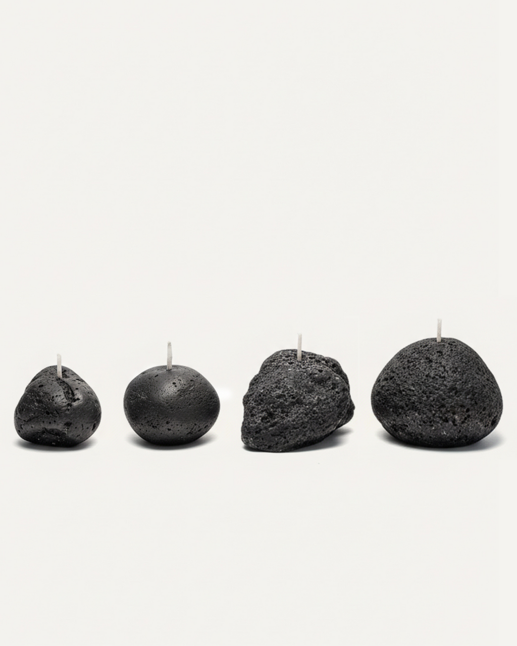 Four volcanic stone candles with textured surfaces arranged on a white background