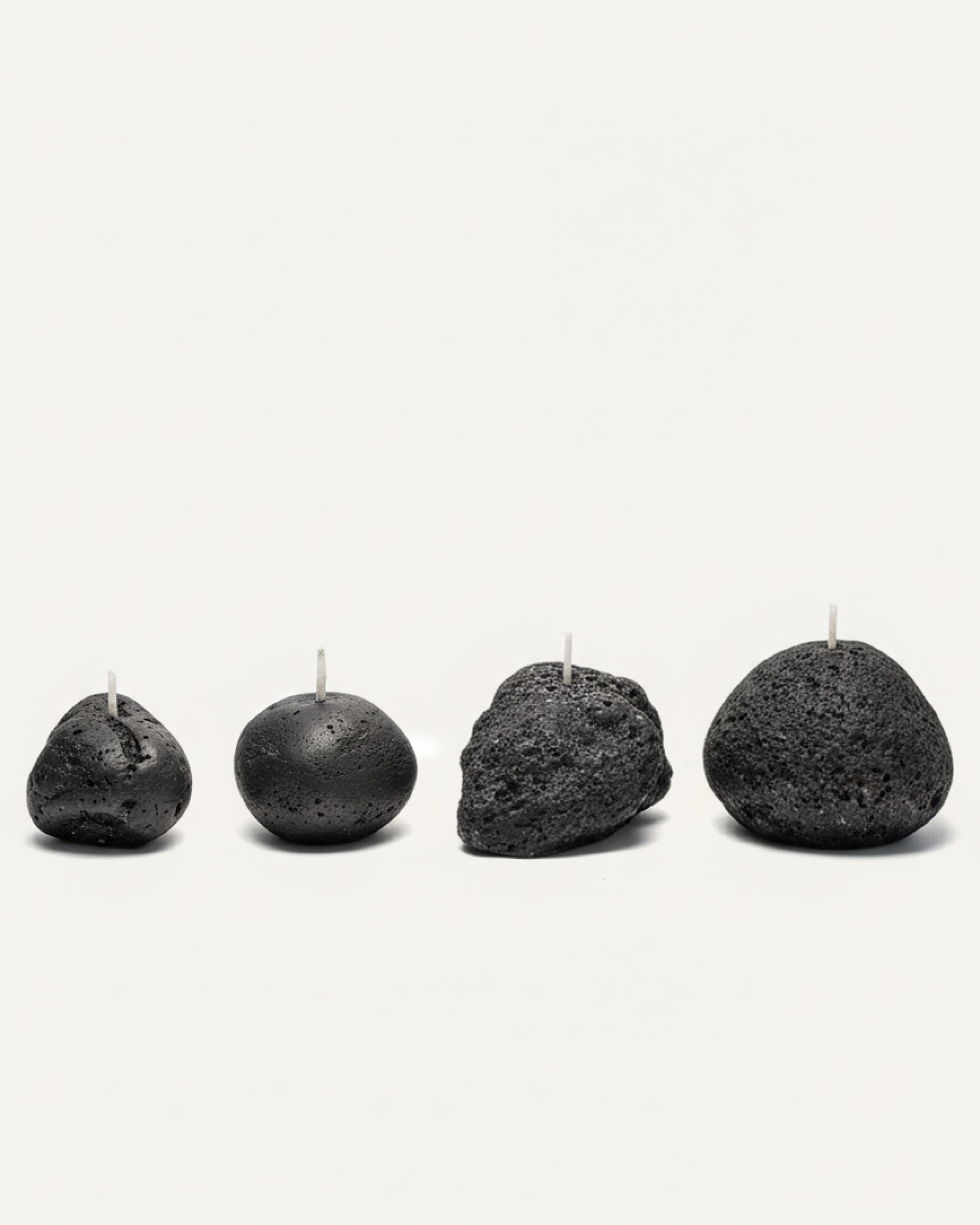 Four volcanic stone candles with textured surfaces arranged on a white background
