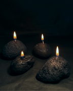 Four volcanic stone candles with lit wicks arranged on a dark surface