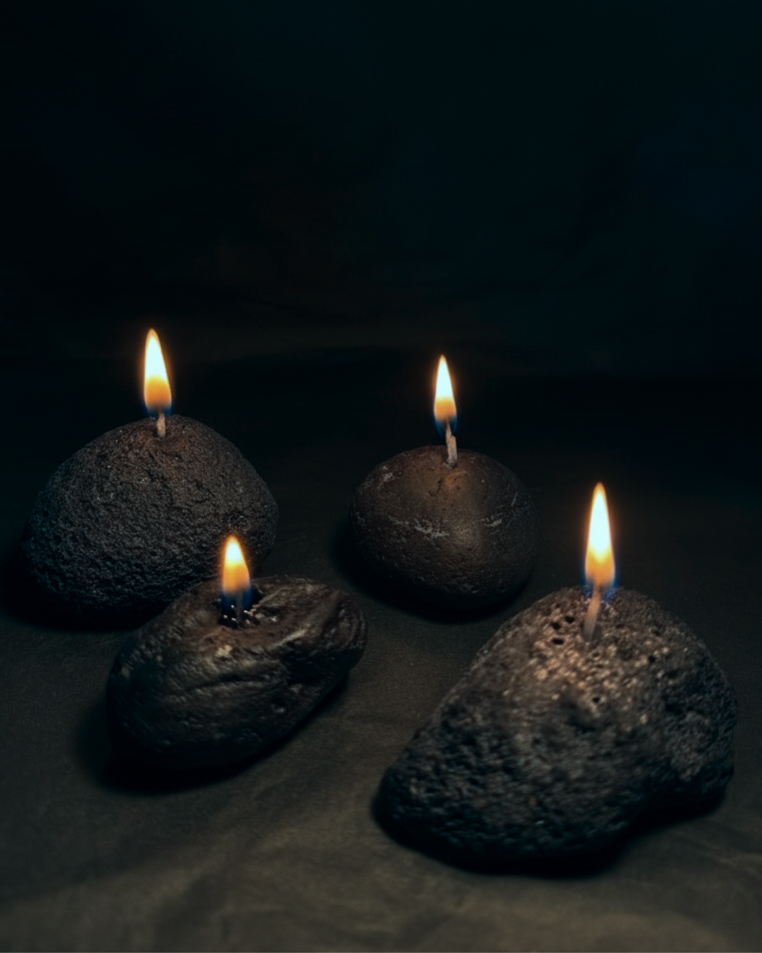 Four volcanic stone candles with lit wicks arranged on a dark surface
