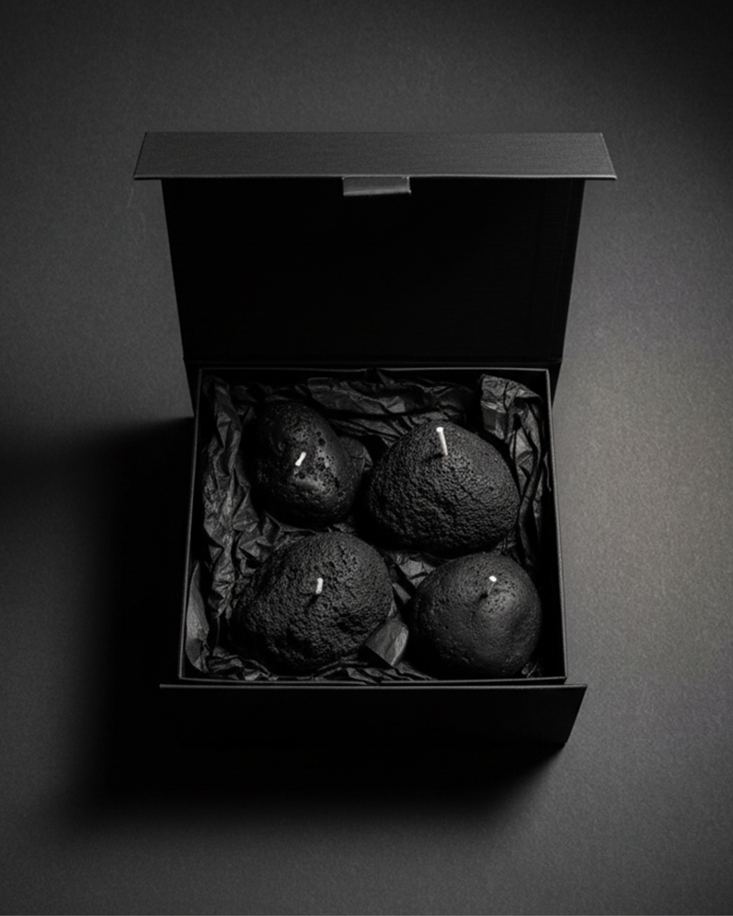 Set of four volcanic stone candles arranged in a black gift box on a dark background